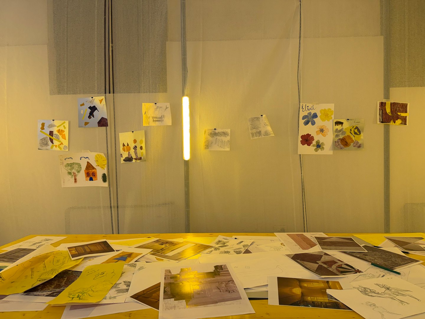 Creative workspace with art supplies on a wooden table and colorful drawings on the wall.